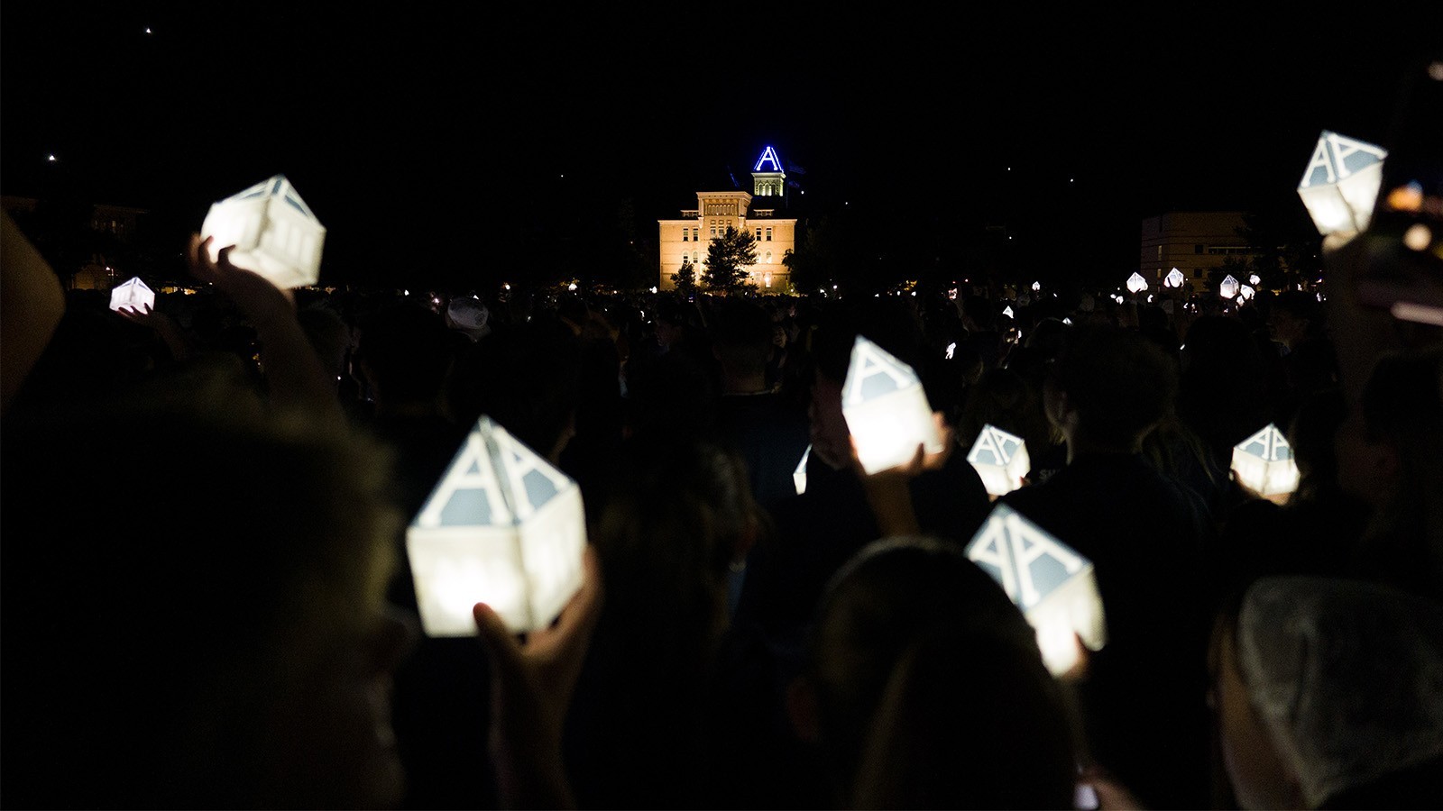 Students holding up lanterns shaped like the Old Main tower at night on USU Logan's Quad.