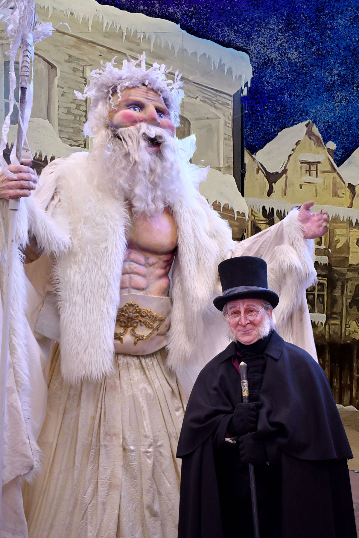 A larger-than-life puppet posing with an actor playing Ebenezer Scrooge.