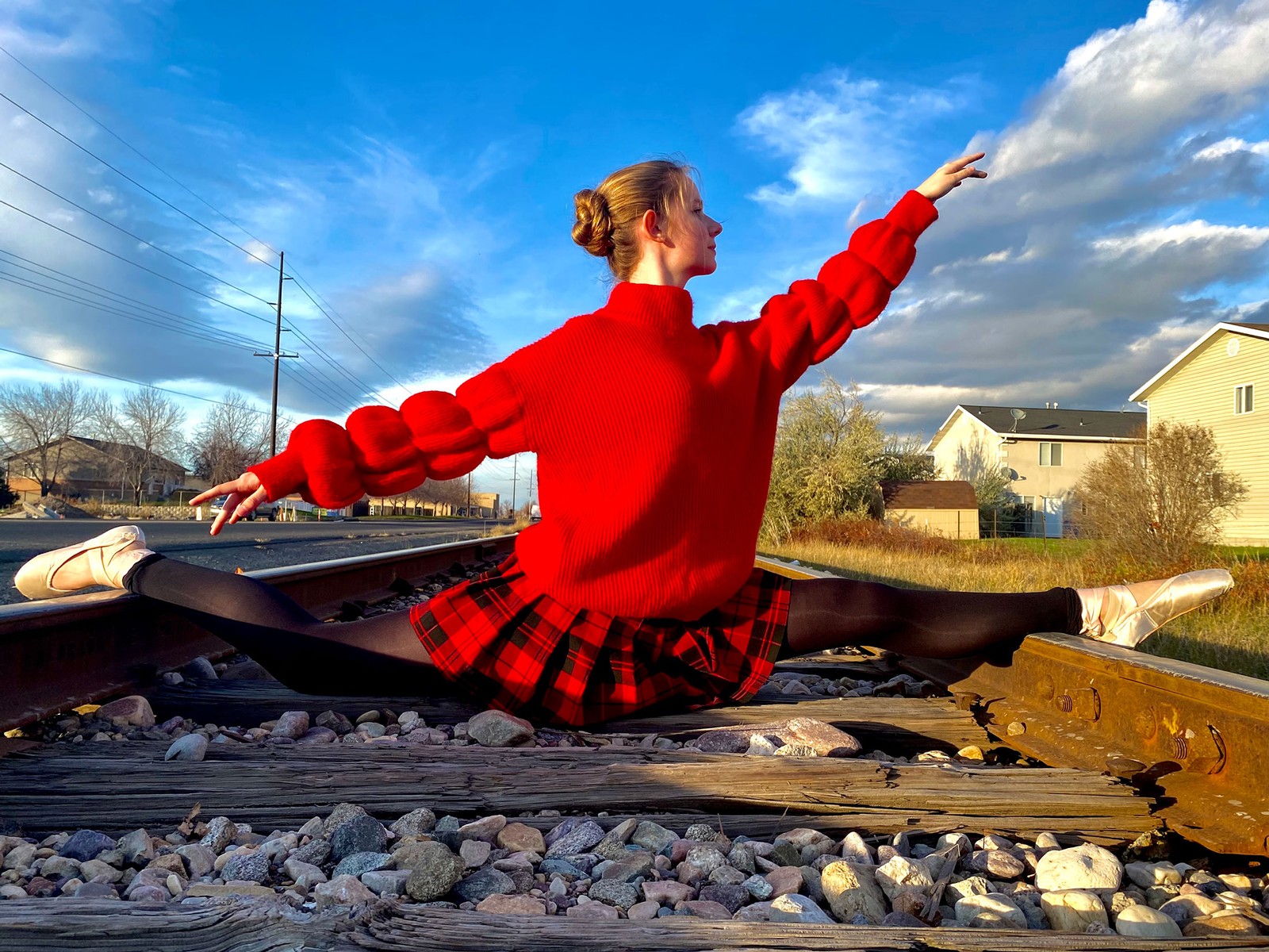 A woman wearing ballerina pointe shoes does the splits across railroad tracks.