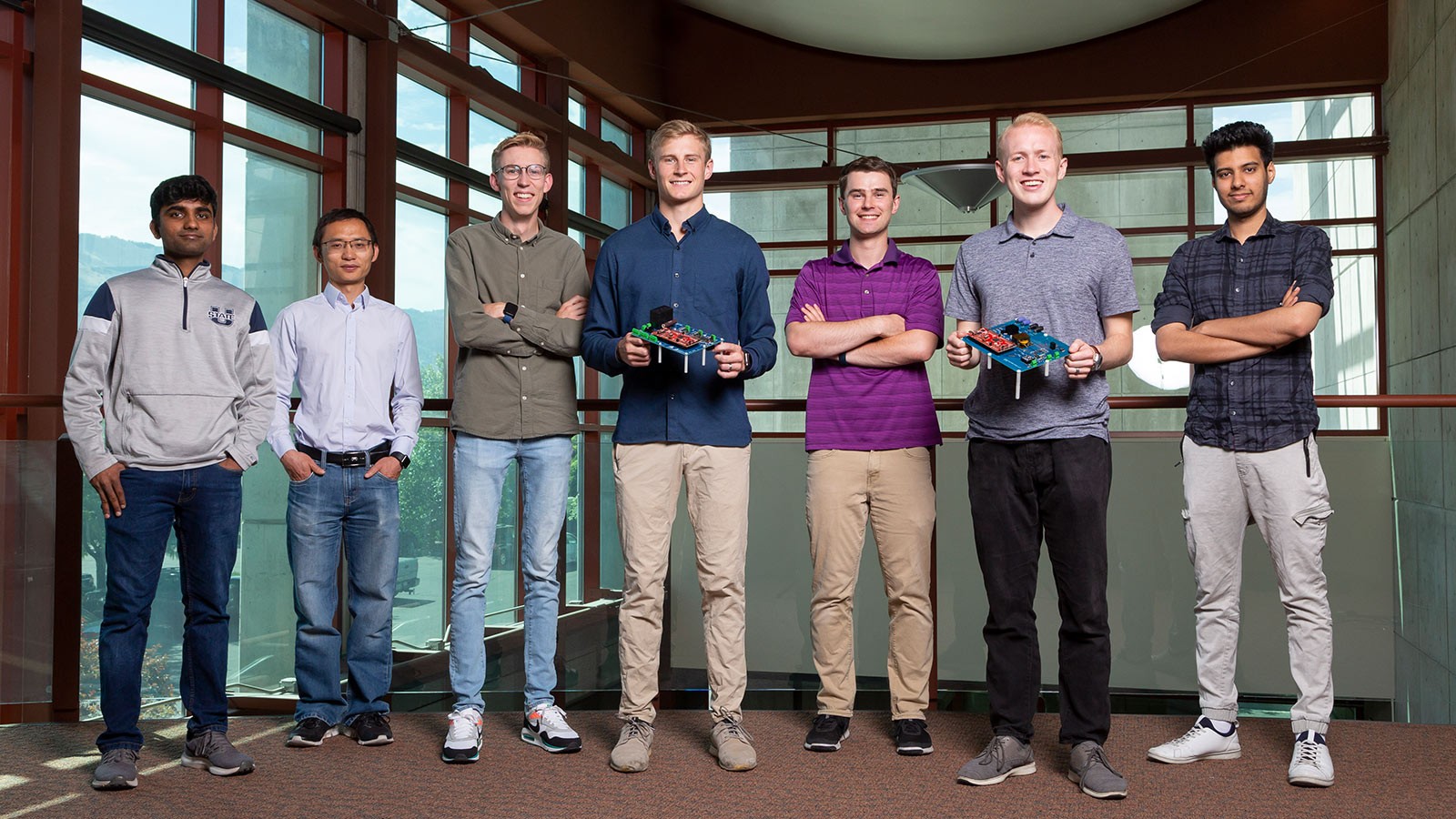 Seven engineering students pose for a picture. Two hold electrical devices.