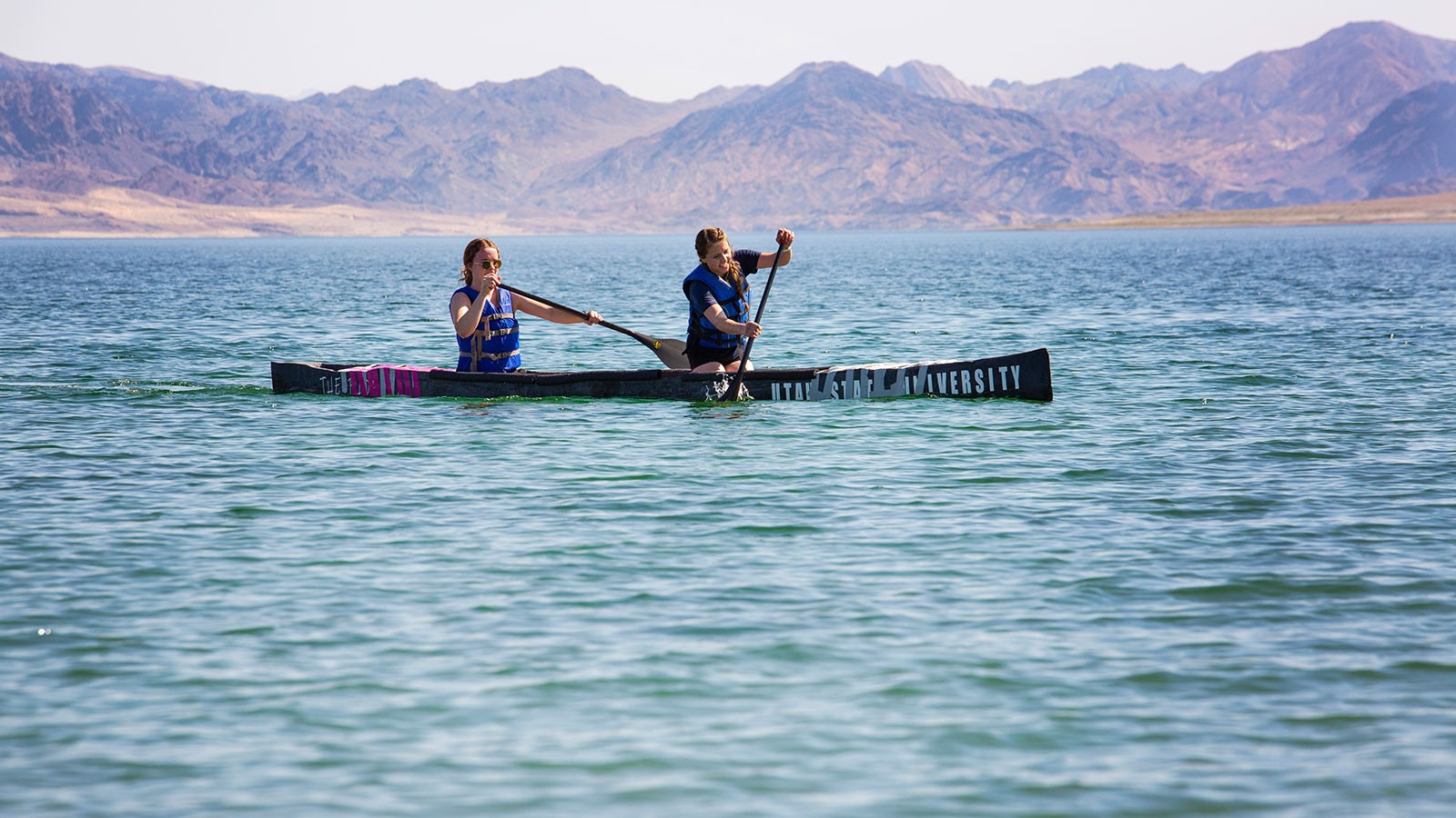 Two students paddle a canoe made of concrete across a lake.