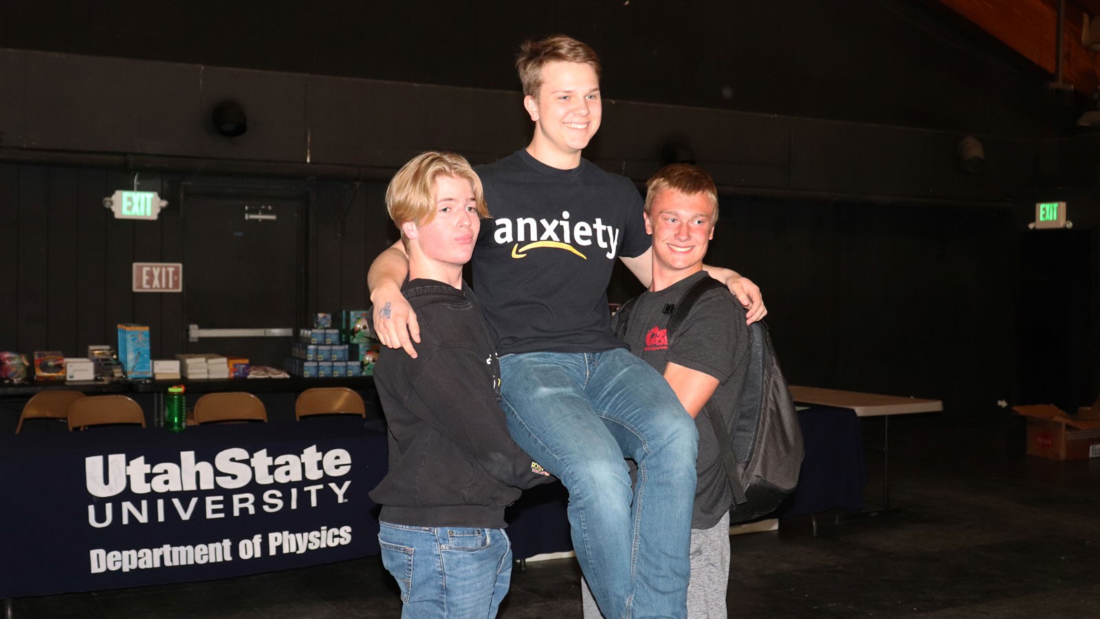 Two high school students form a chair with their arms to hold an uplifted third high school student.