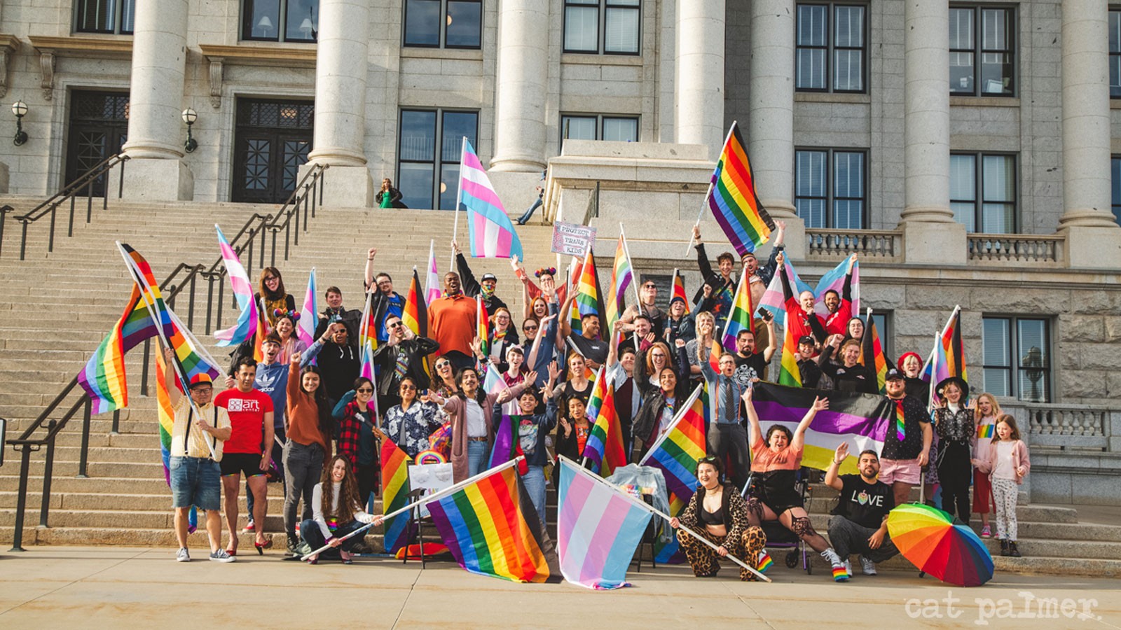 People hold Pride flags as they stand on the steps of the Utah Capitol.
