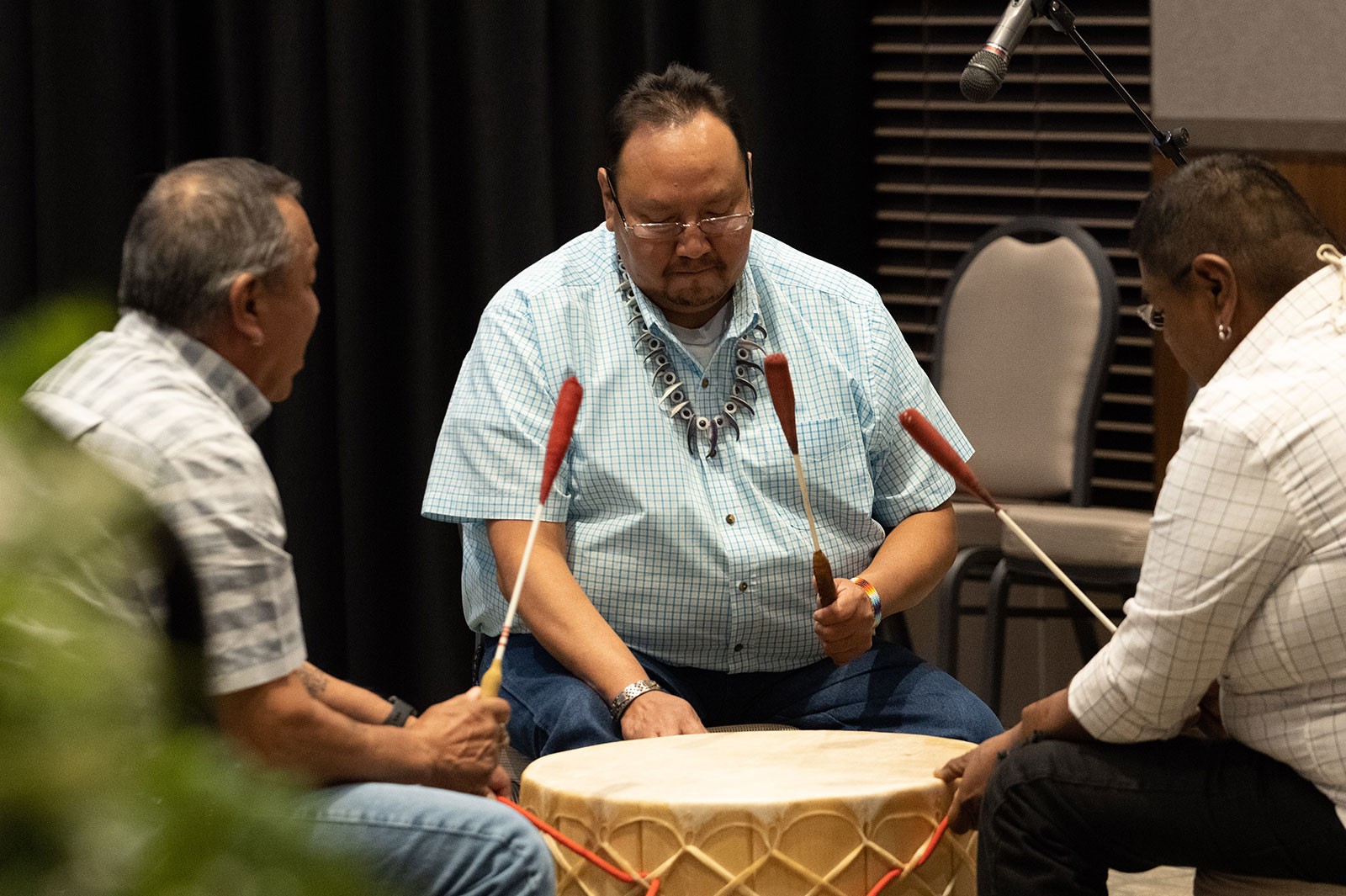 Three men play a drum.