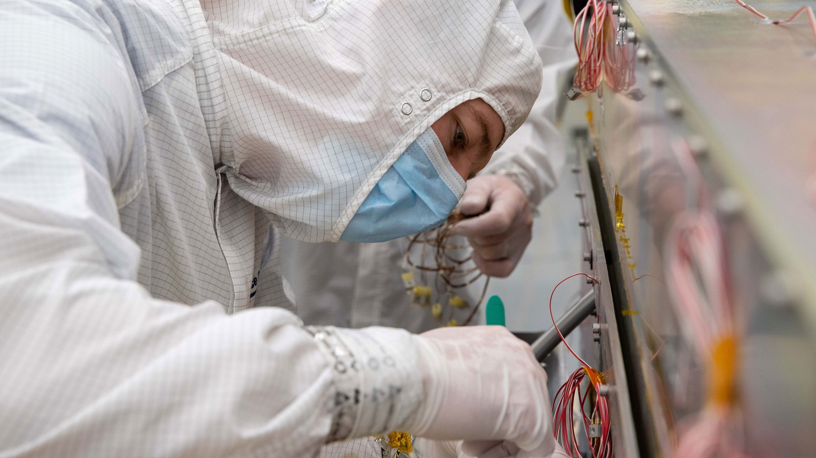 A person wearing protective equipment works on a scientific instrument.