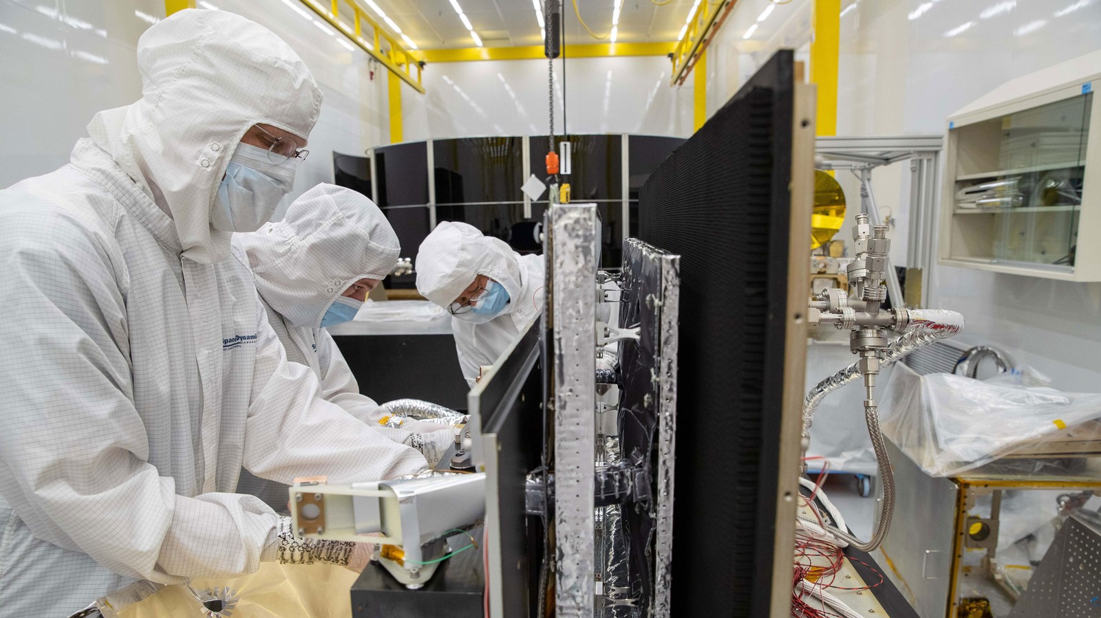 People wearing protective equipment work on a scientific instrument.