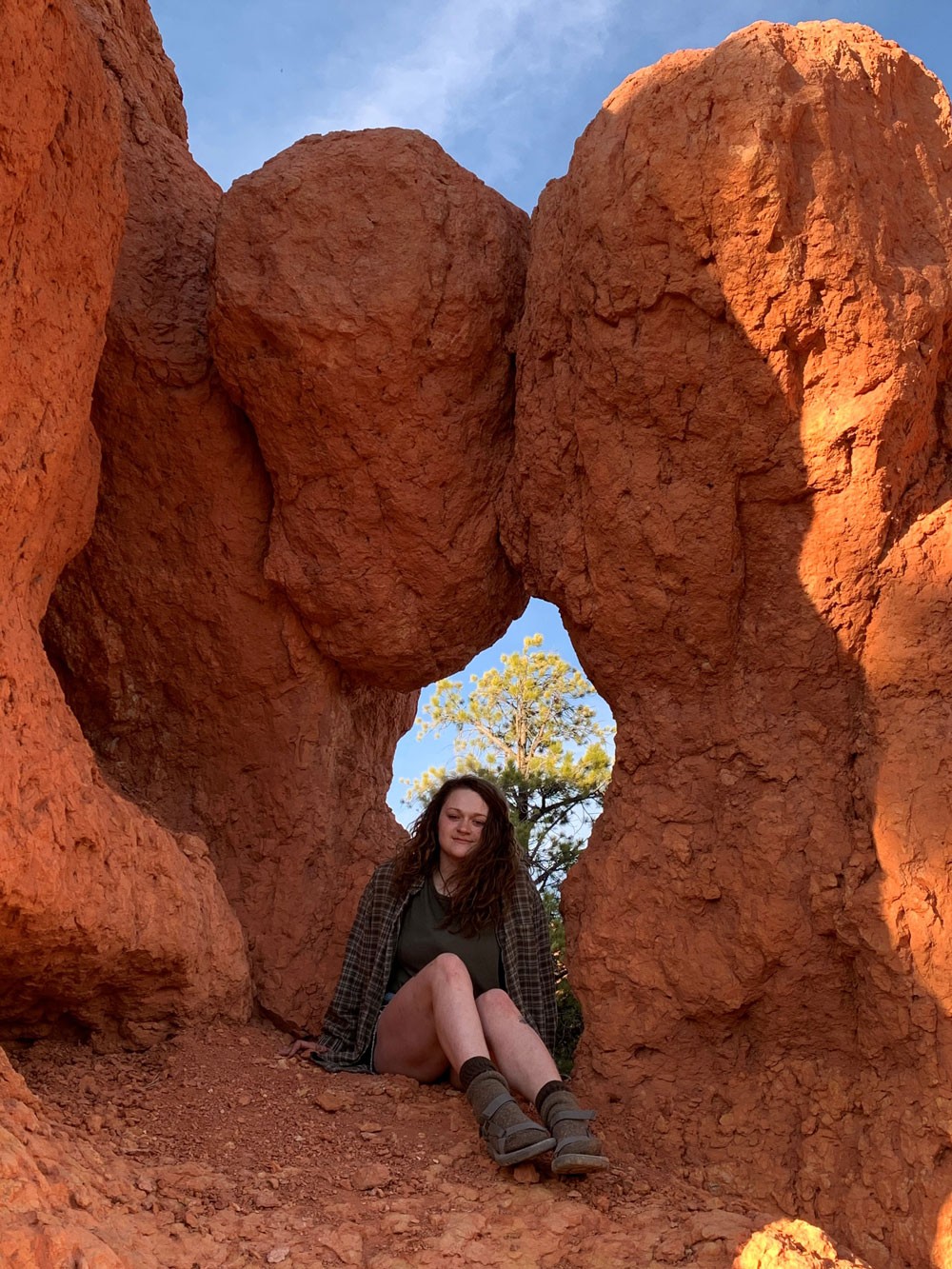 Alli Riebel sits in front of a natural window in a redrock formation.