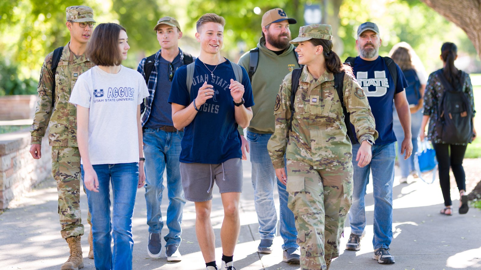 Students in USU apparrel and military fatigues walk on the Logan campus.