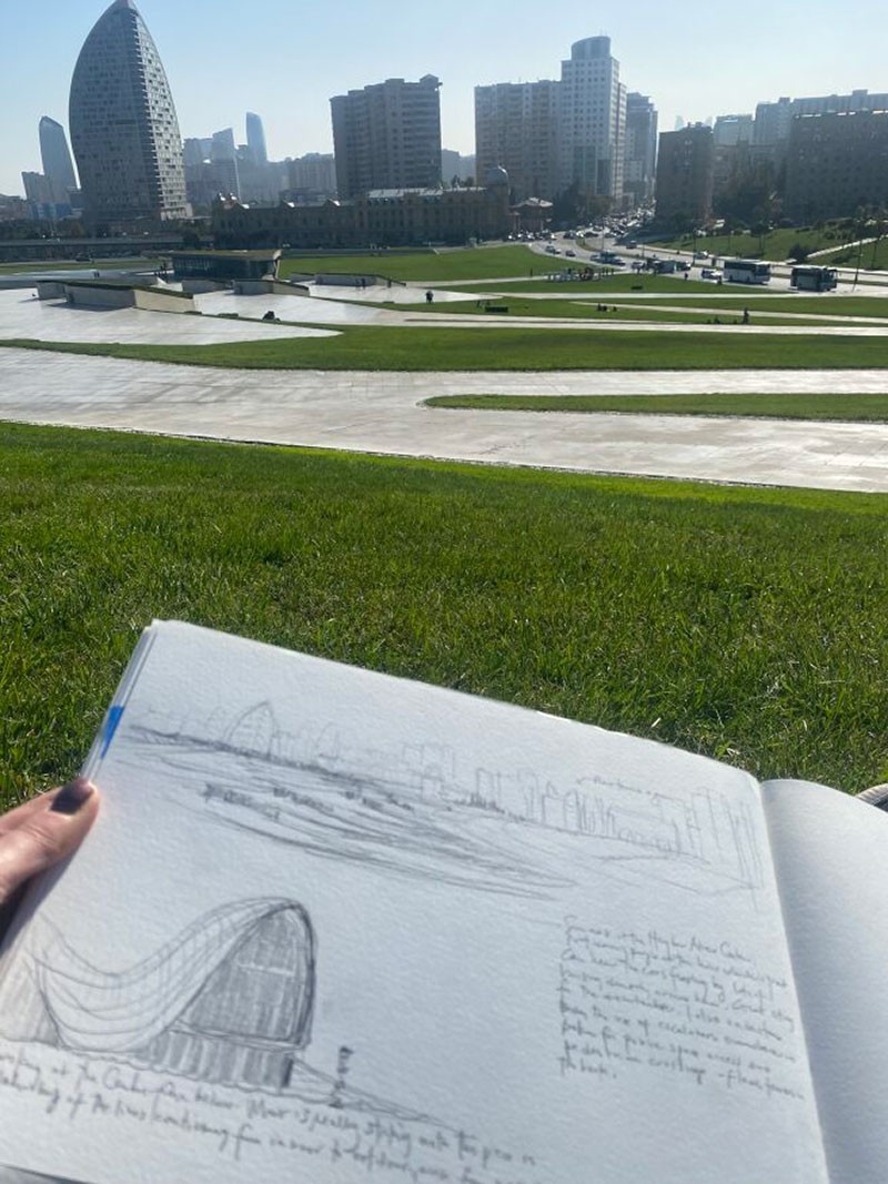 A person holding a sketchbook with a park in the background.