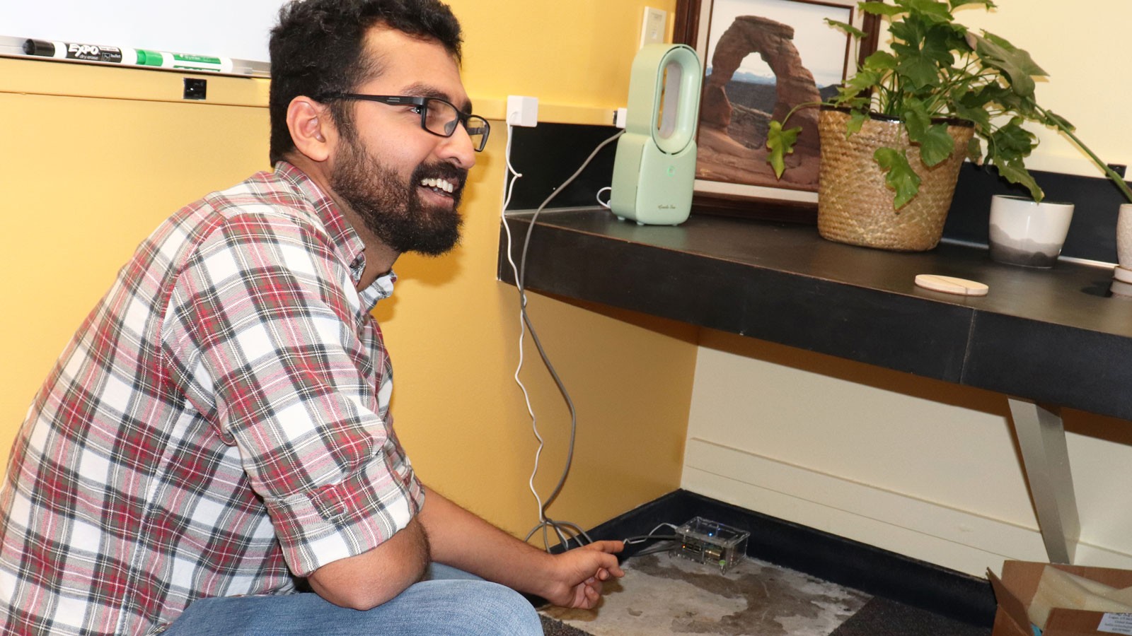 A scientist pointing to a small electronic device on the floor.
