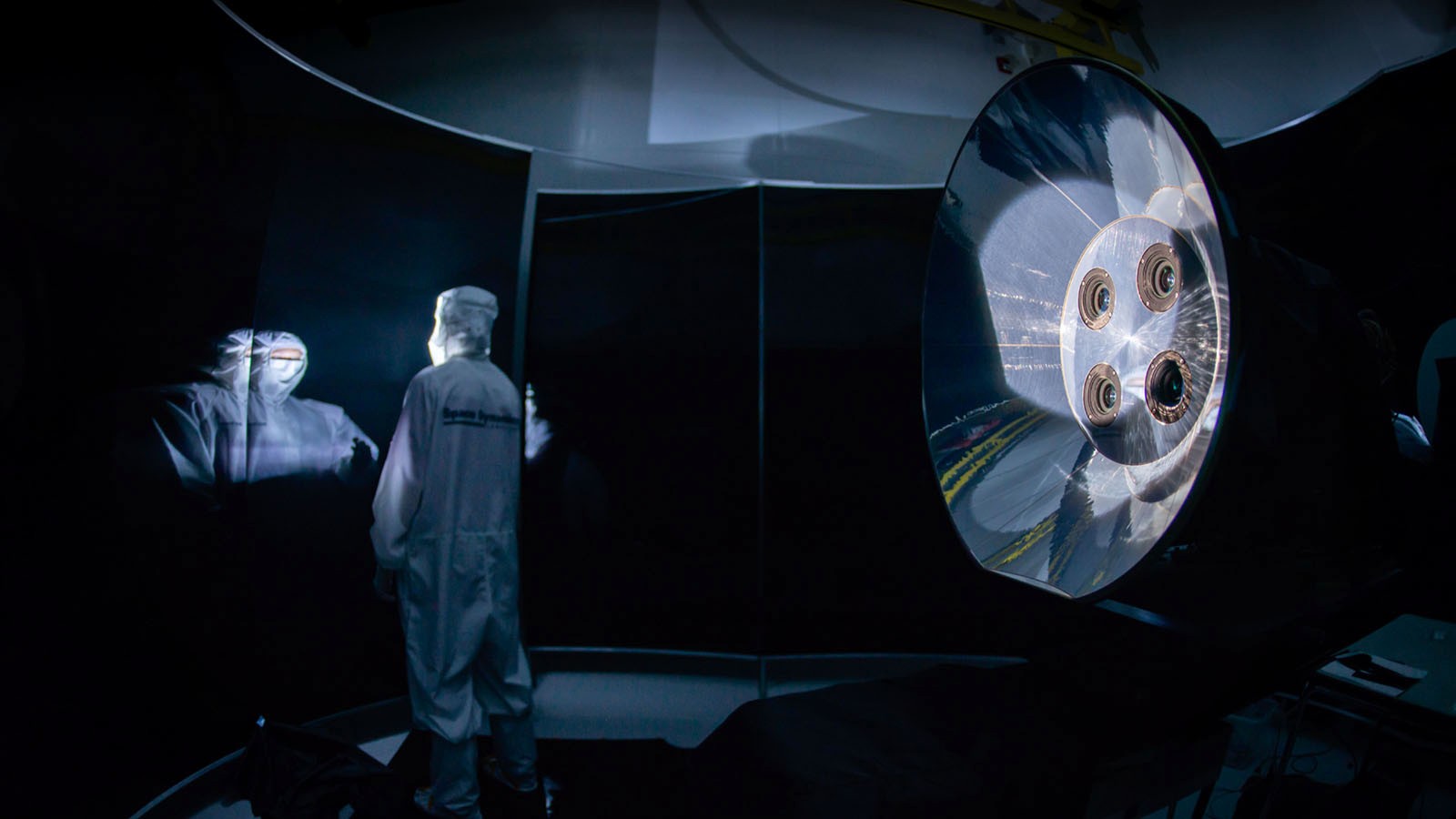 An engineer in protective equipment working on a space telescope.