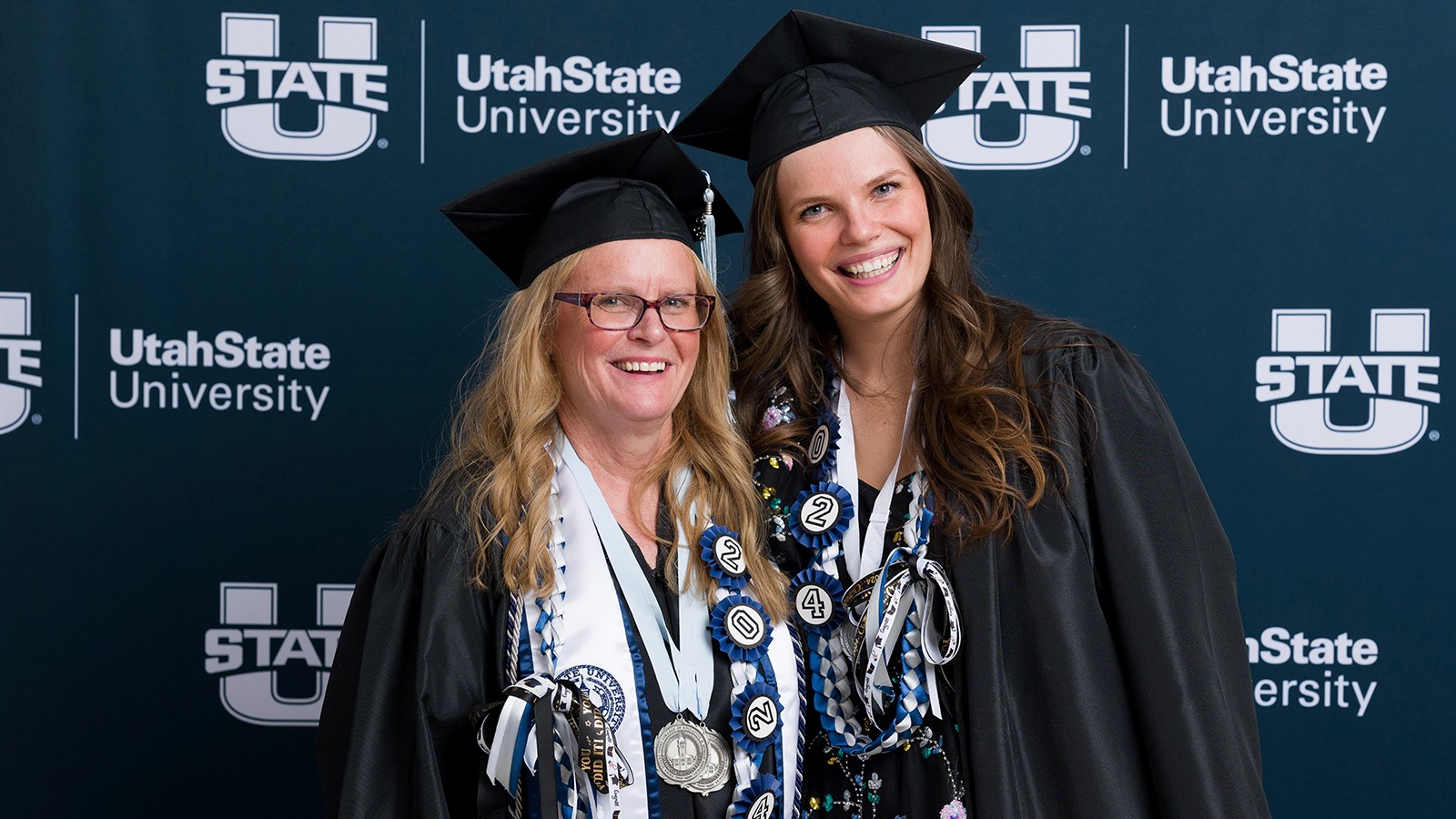 Two women stand together in graduation regalia.