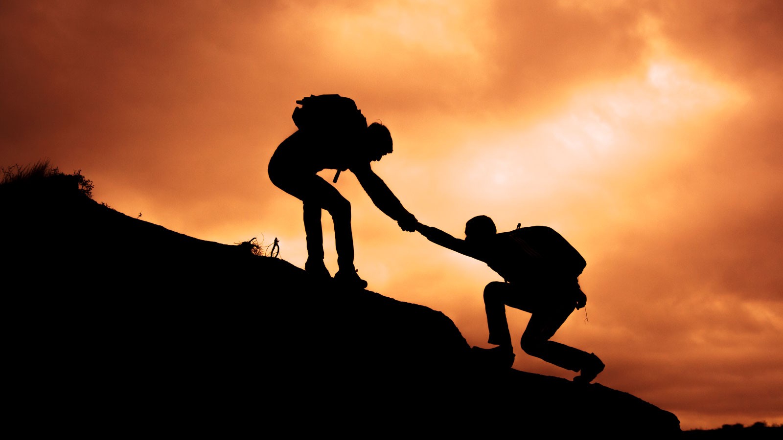 A hiker taking a fellow hiker by the hand to help them up.