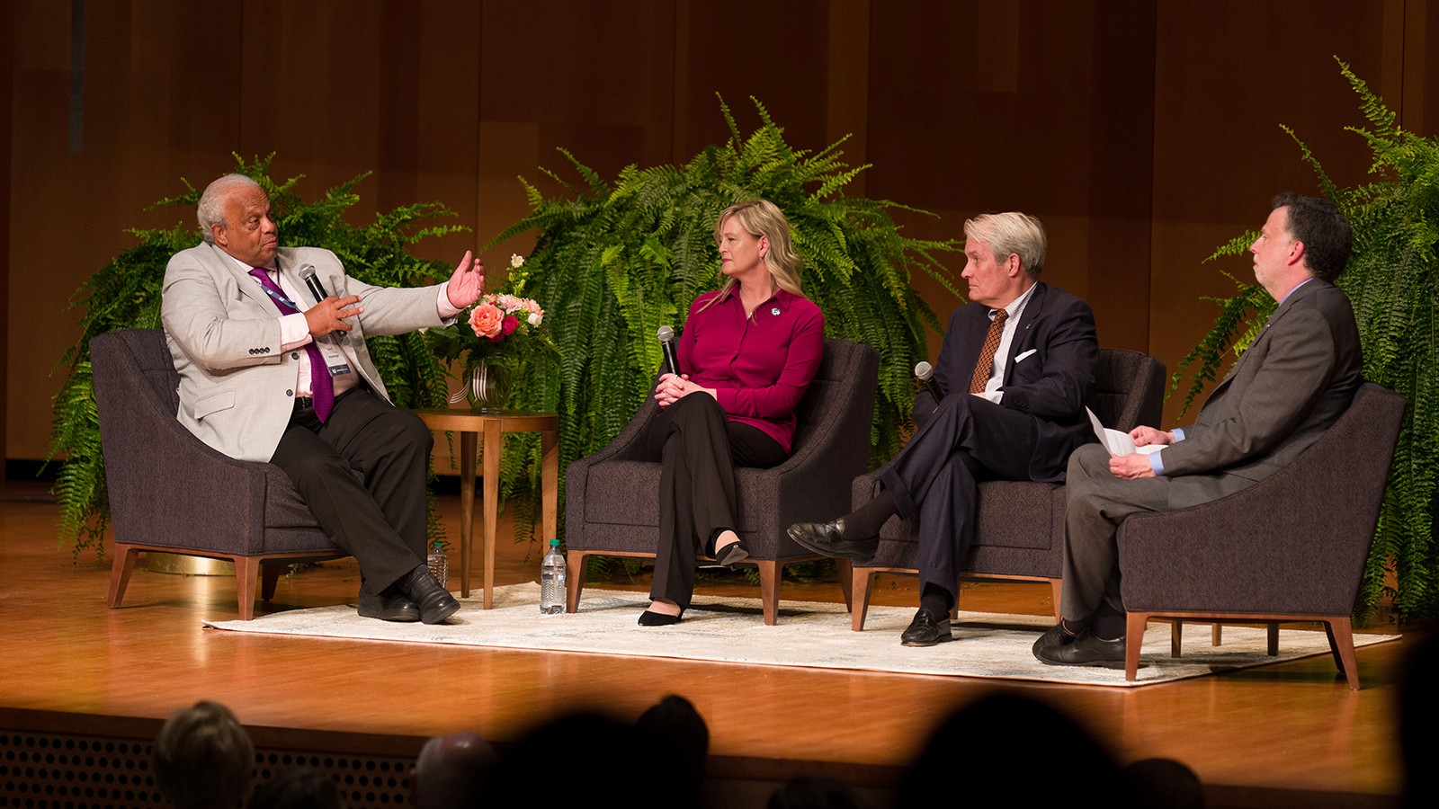 Four people sit in chairs in an auditorium.