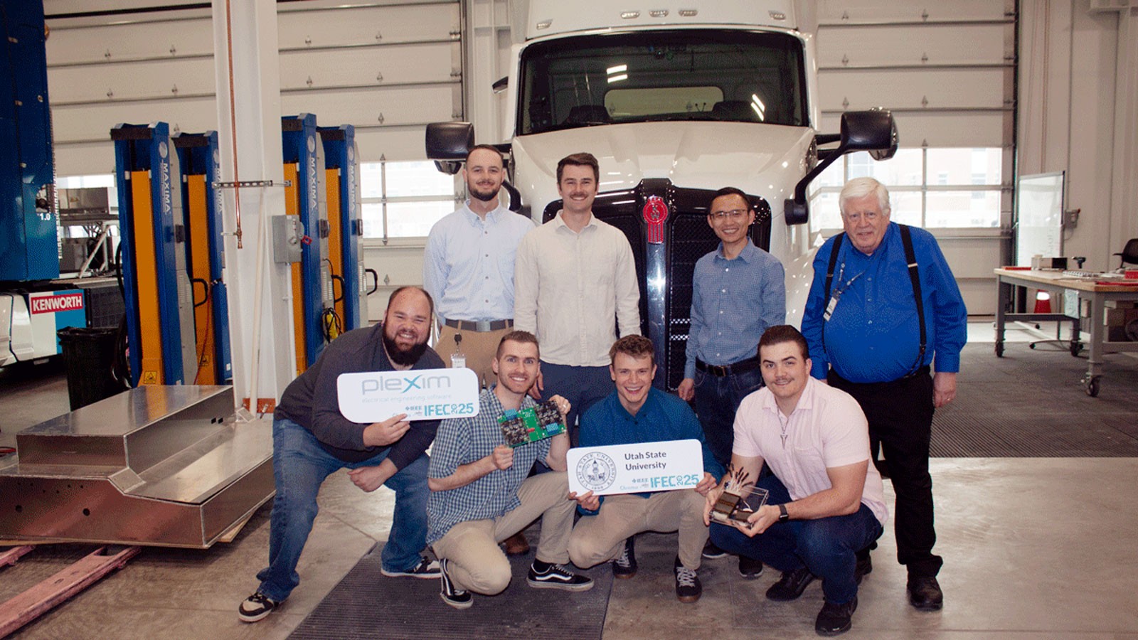 A team of engineers standing in front of a semi tractor in a garage.