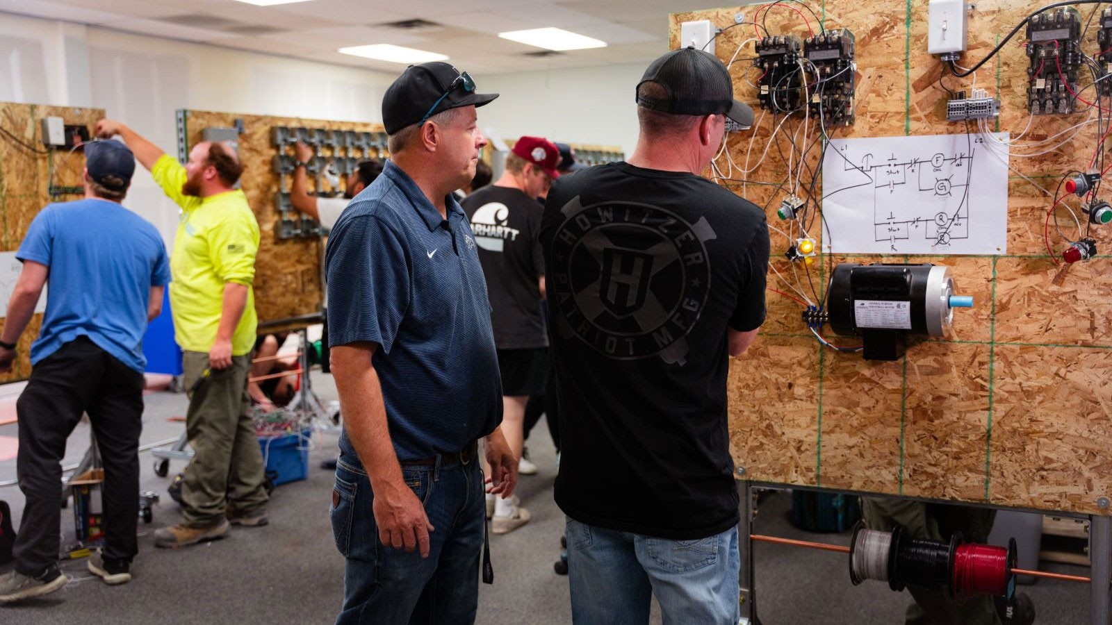 Students and instructors examining circuits built from electrical components on plywood.