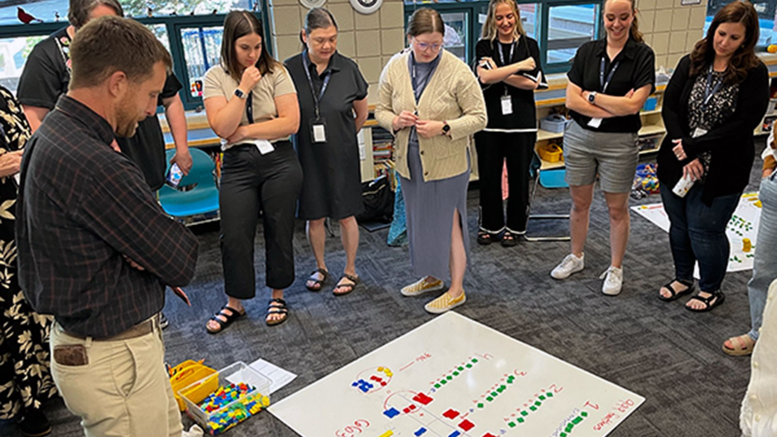 Teachers standing in a classroom, looking at a math visual aid on the floor.