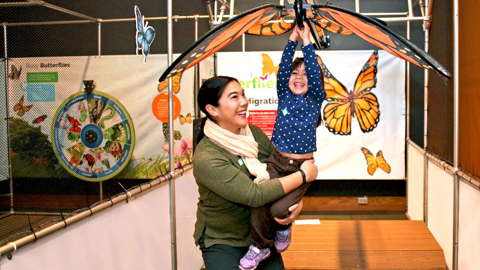 An adult helping a child ride a zipline with butterfly wings.