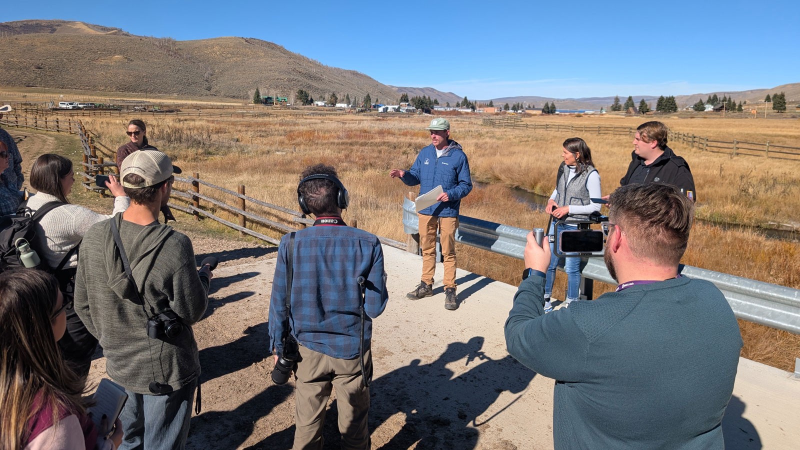 People recording a man speaking near a creek.