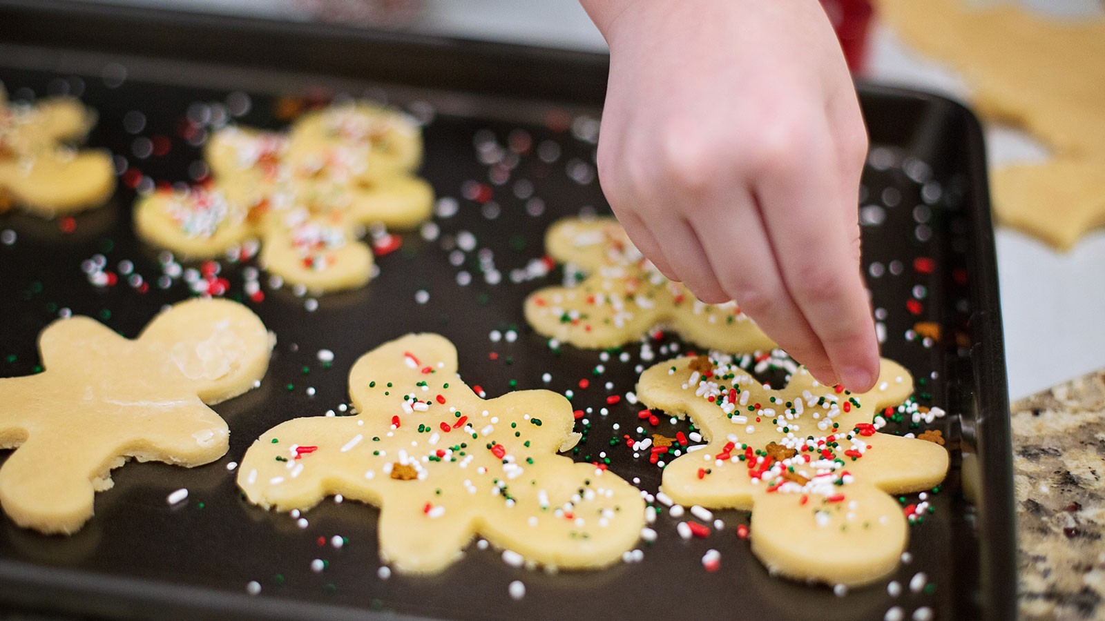 A person putting sprinkles on cookies.