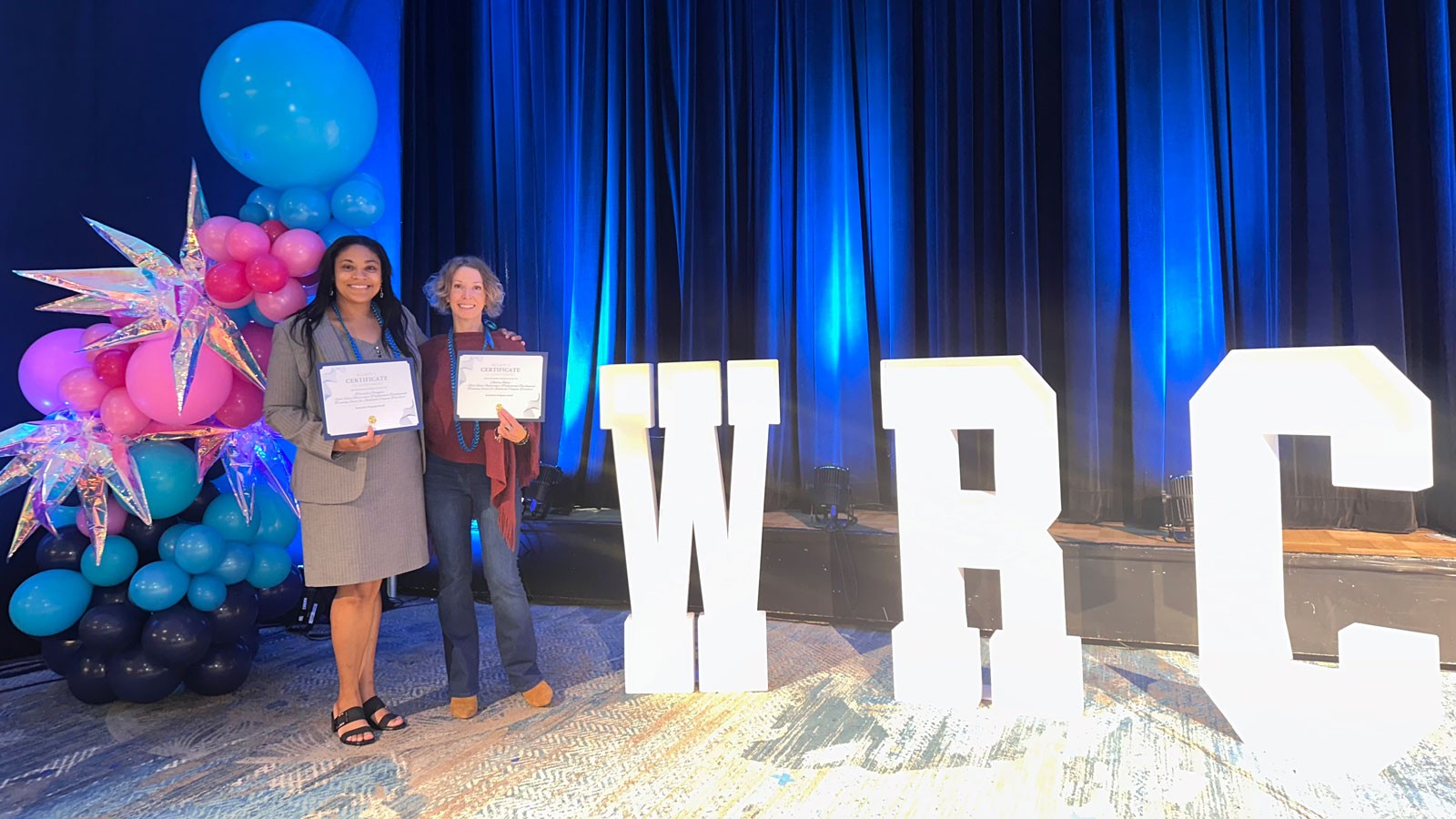 Two people holding awards at a ceremony.
