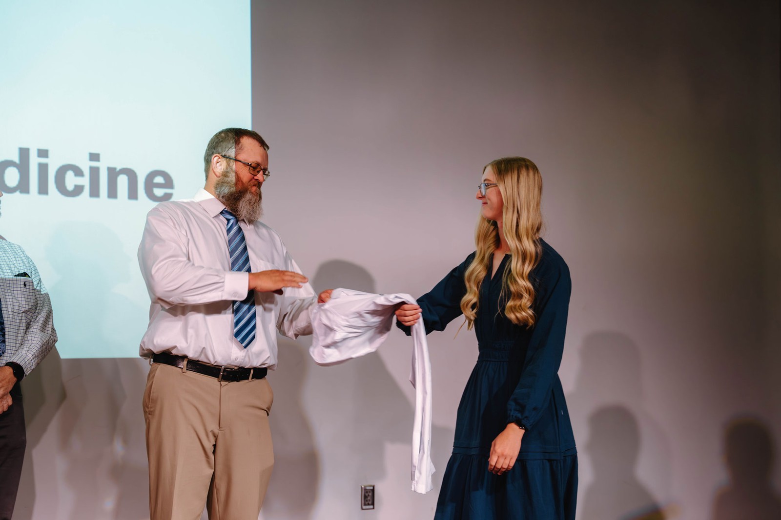 A man handing a woman a white coat on stage at an event.