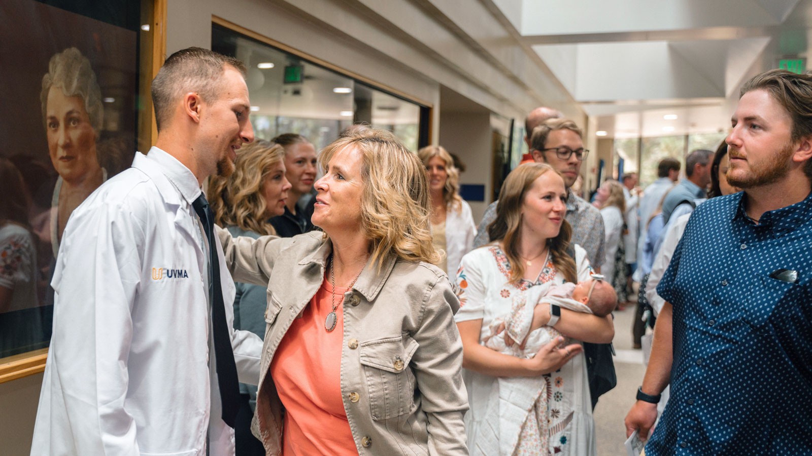 People congratulating students in white coats after a ceremony.