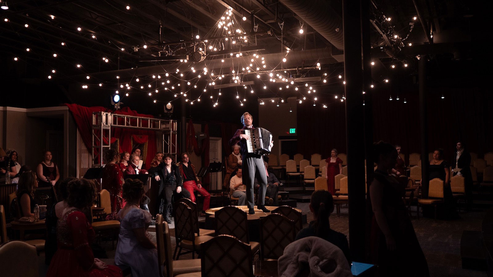 People watching an actor play the accordion in a theater-in-the-round.