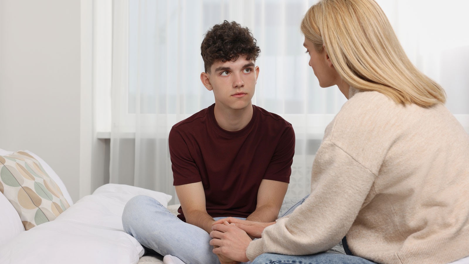 A mother speaking to a teenager in a bedroom.