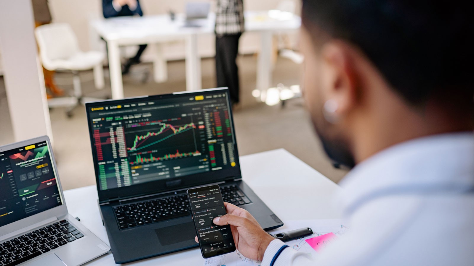 An investor watching stocks on laptops and a cell phone.