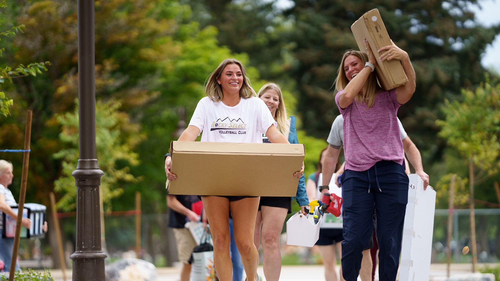 Two women carry boxes as they move things into a dorm room