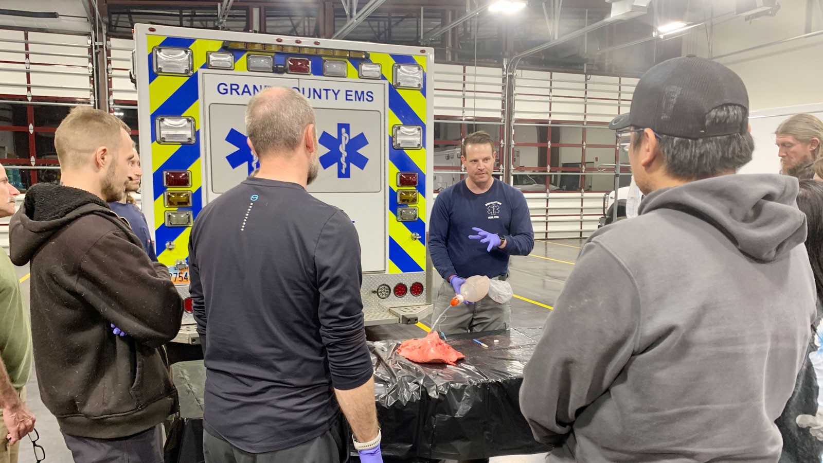 An instructor demonstrates EMT skills in an ambulance garage.