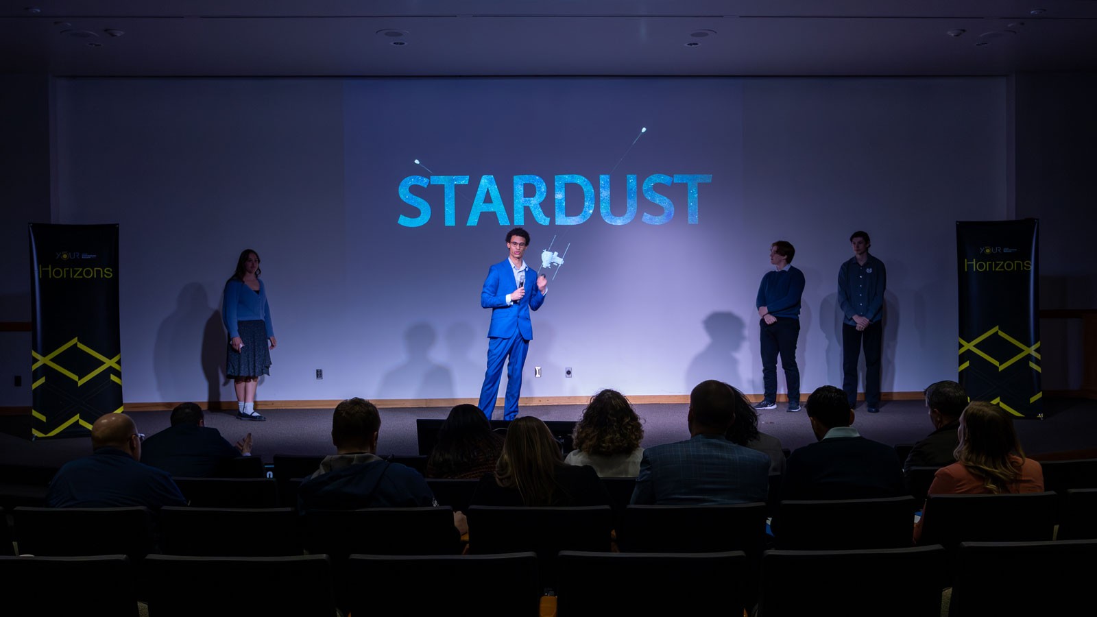 Competitors on stage at a research competition. Text on screen reads "Stardust."