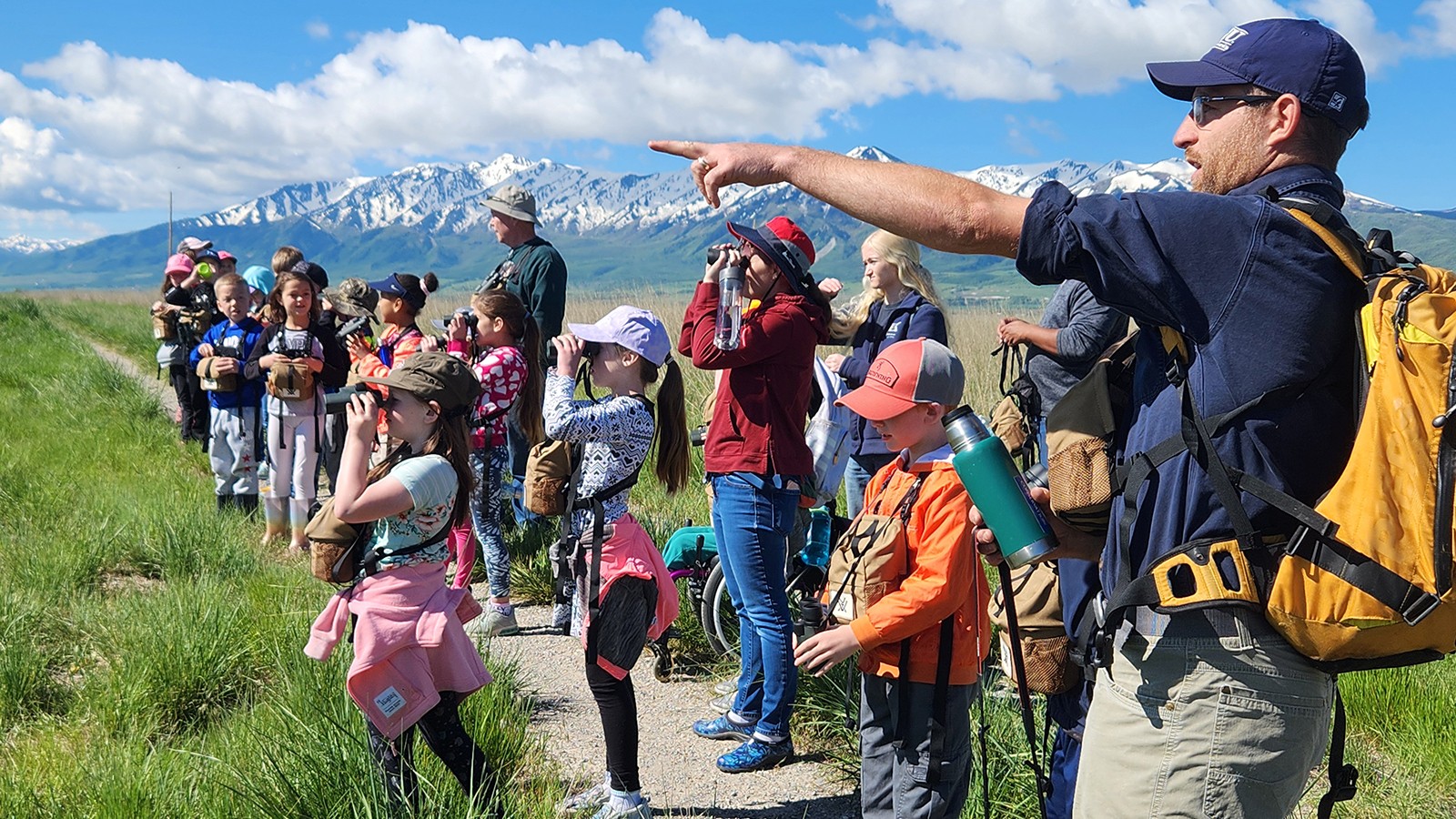 A man points something out while children look through binoculars.