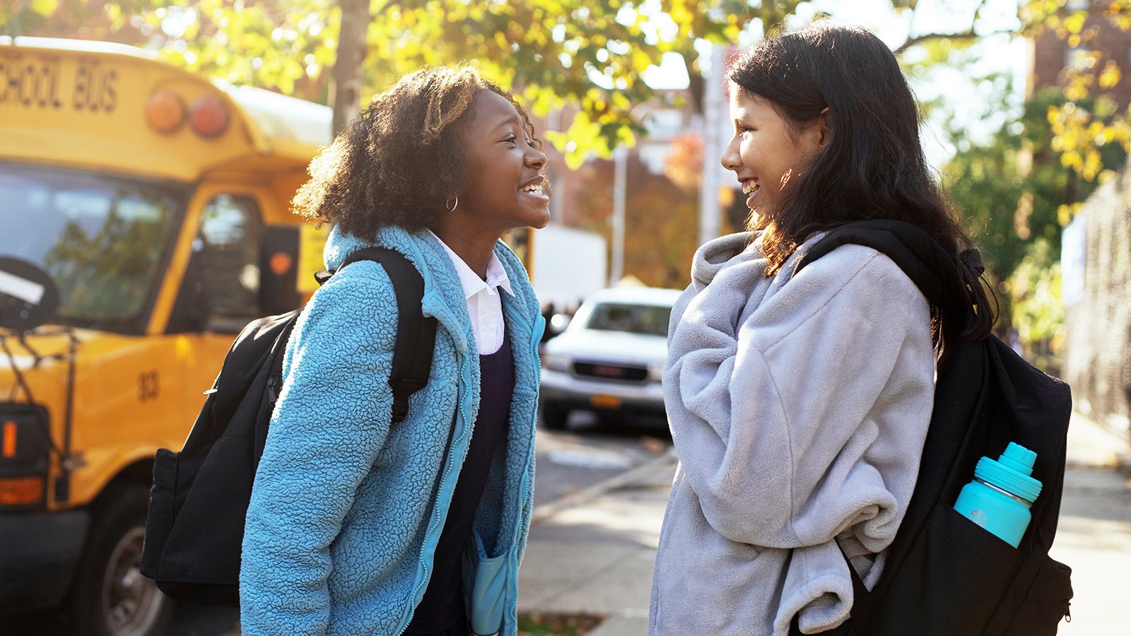 Two adolescent students chatting after getting off the bus.