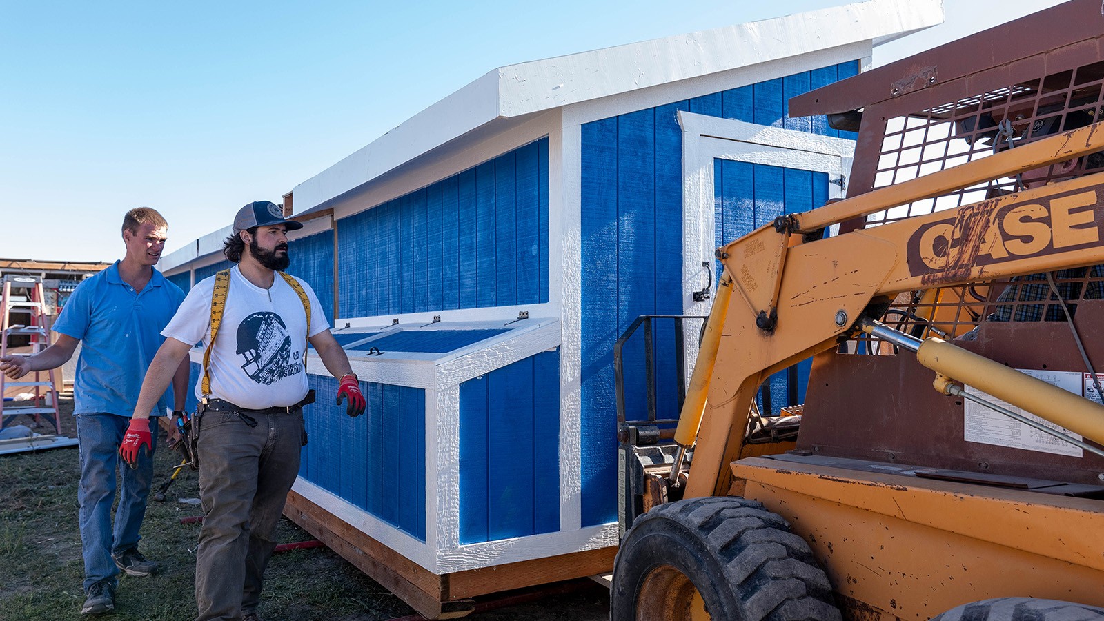 Image shows two men speaking with a skid steer operator