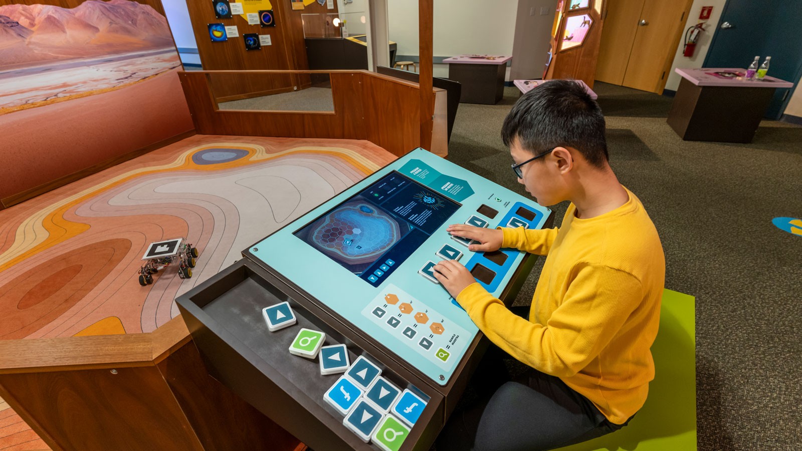 A child using a touchscreen to control a small robotic rover.