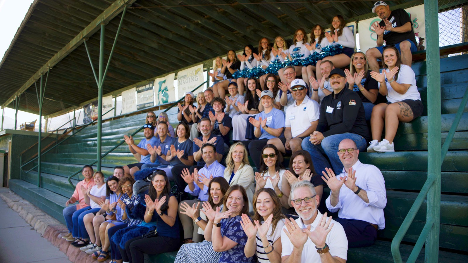 People making an eagle symbol with their hands as they sit in bleachers.