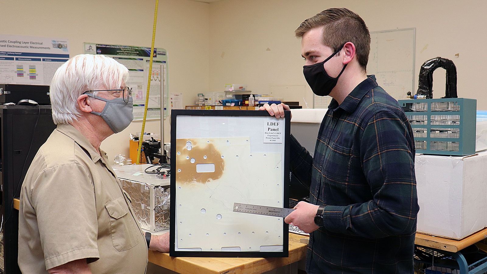 Trace Taylor talks with J.R. Dennison while gesturing to a metal plate in a protective frame.