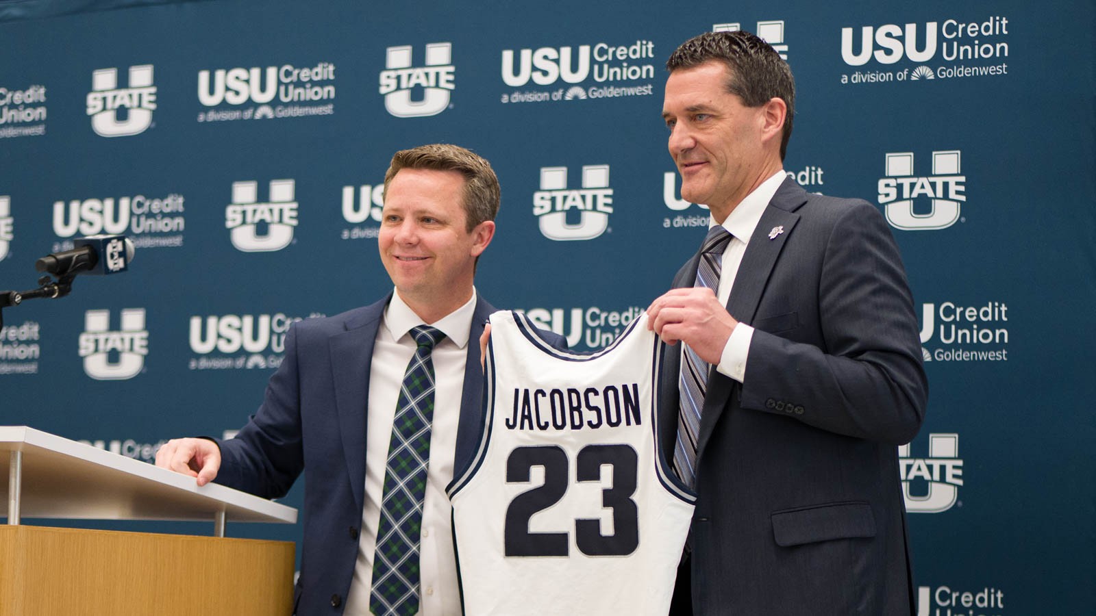 USU AD Cam Walker and new men's basketball coach Ben Jacobson stand together holding a #23 jersey