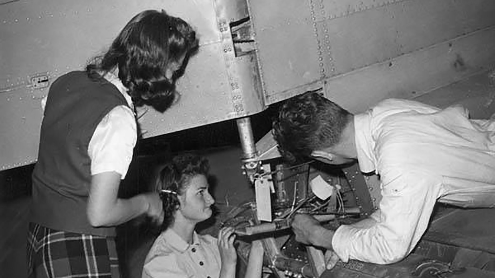 Two female and one male student working on the rear of an airplane, 1940s.