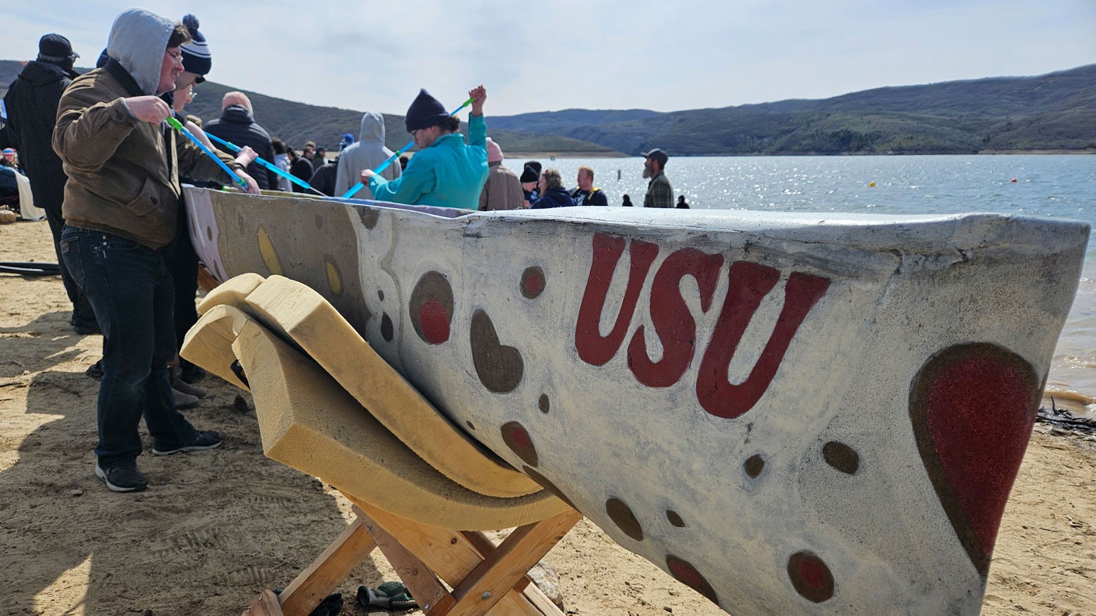 Students working with a canoe made of concrete painted with the letters "USU."