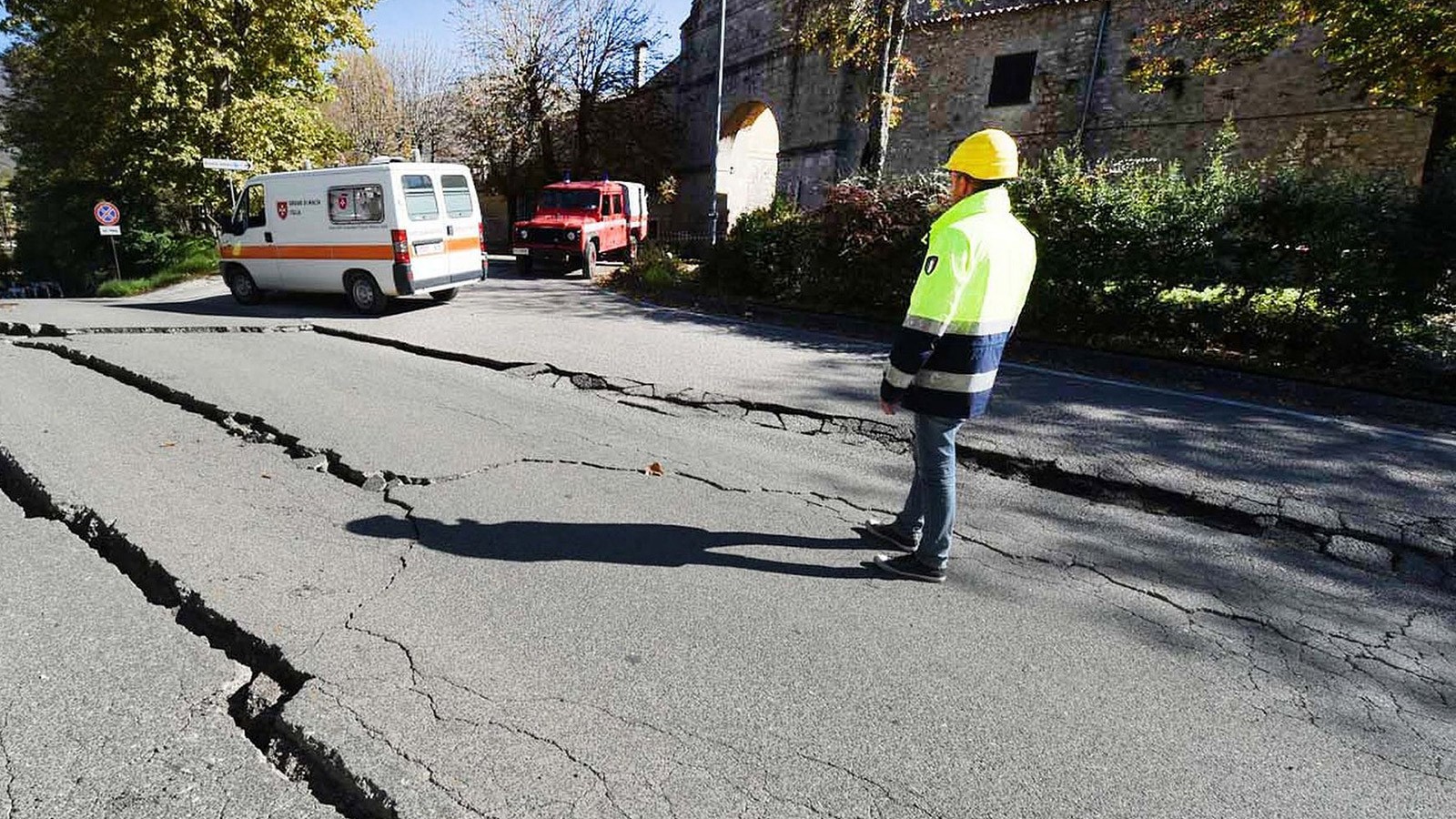 cracked asphalt in a road as utility inspector looks on.