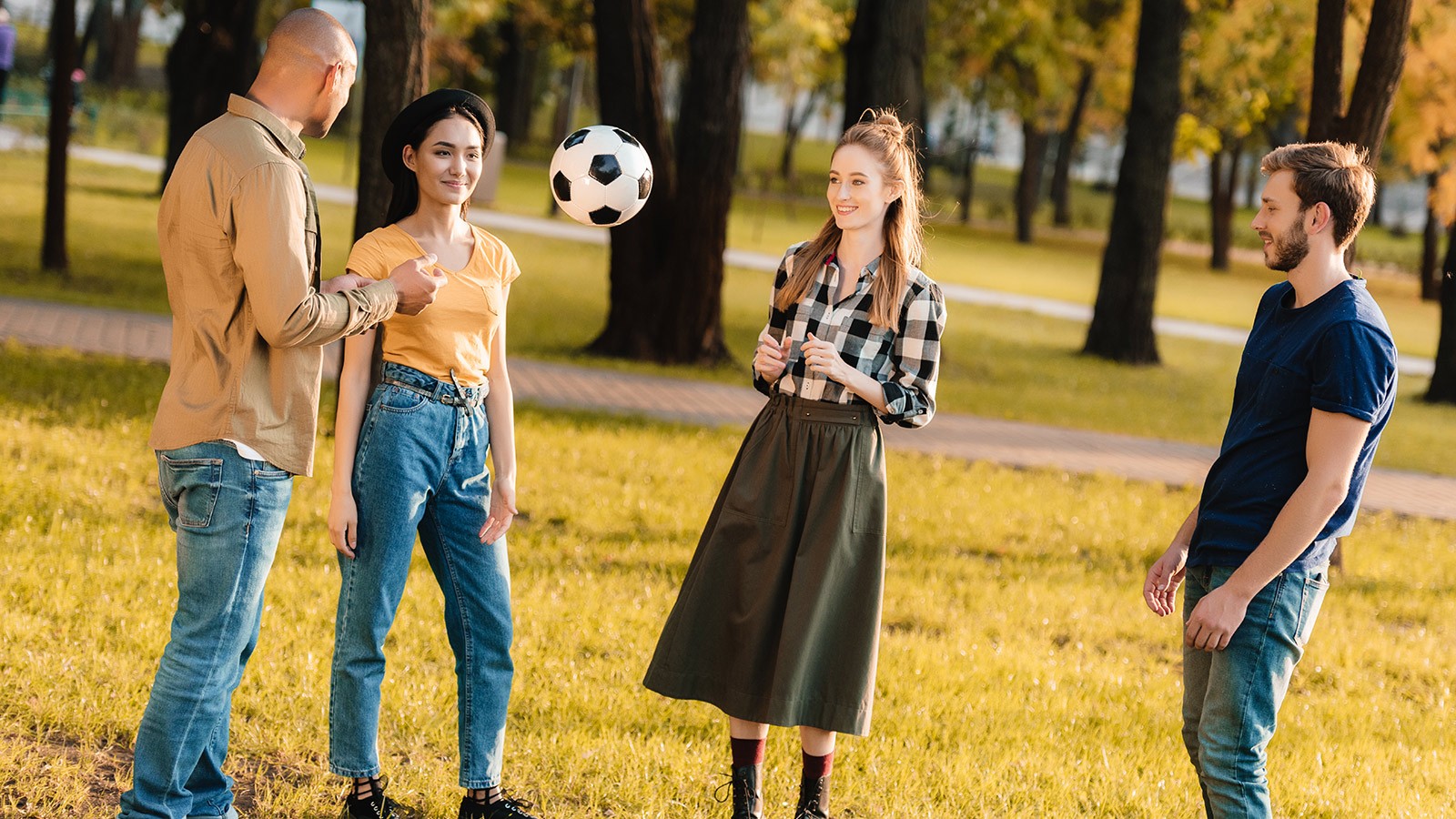 Young adults playing with a soccer ball at a park.