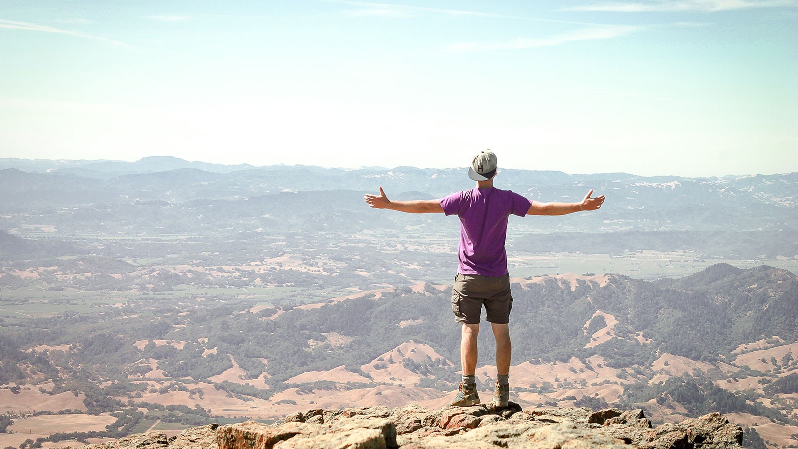 young man standing on a mountain and overlooking a valley.