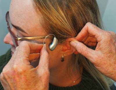 Somone placing a hearing aid onto the ear of a woman