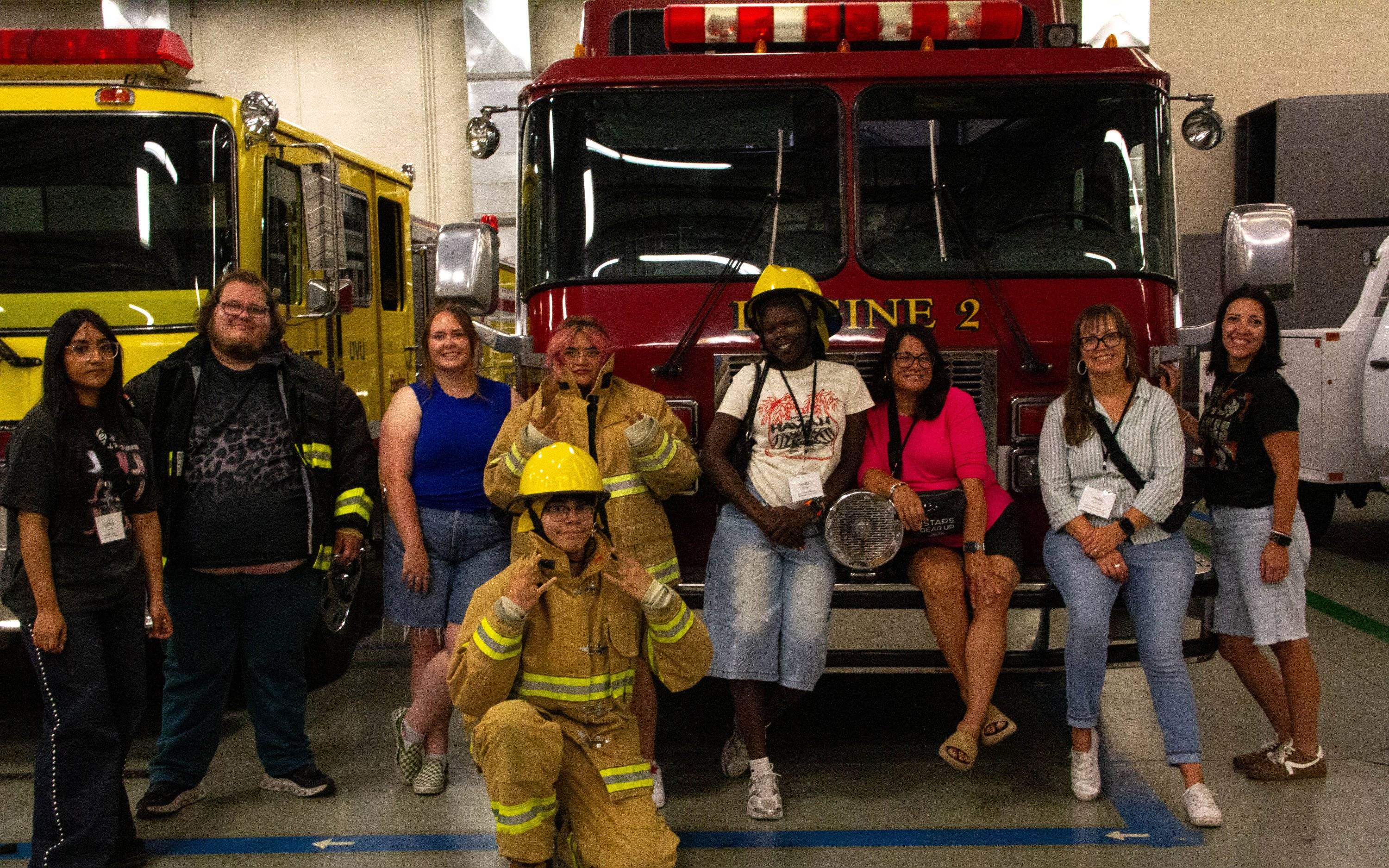 students and advisors standing in front of two fire trucks, and three students are wearing firefighter gear