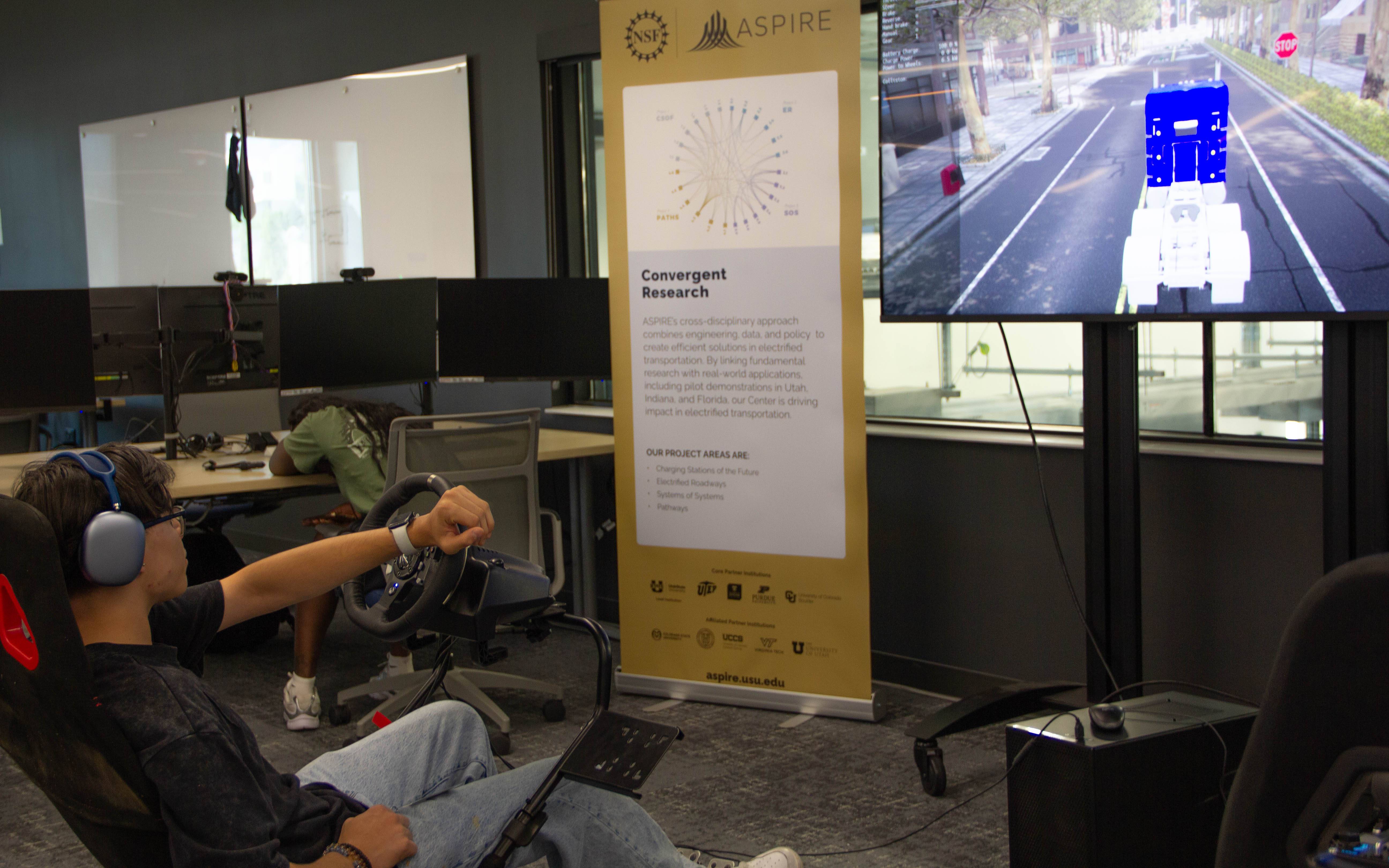 student seated in a simulator chair, looking at a screen as they drive a simulated truck