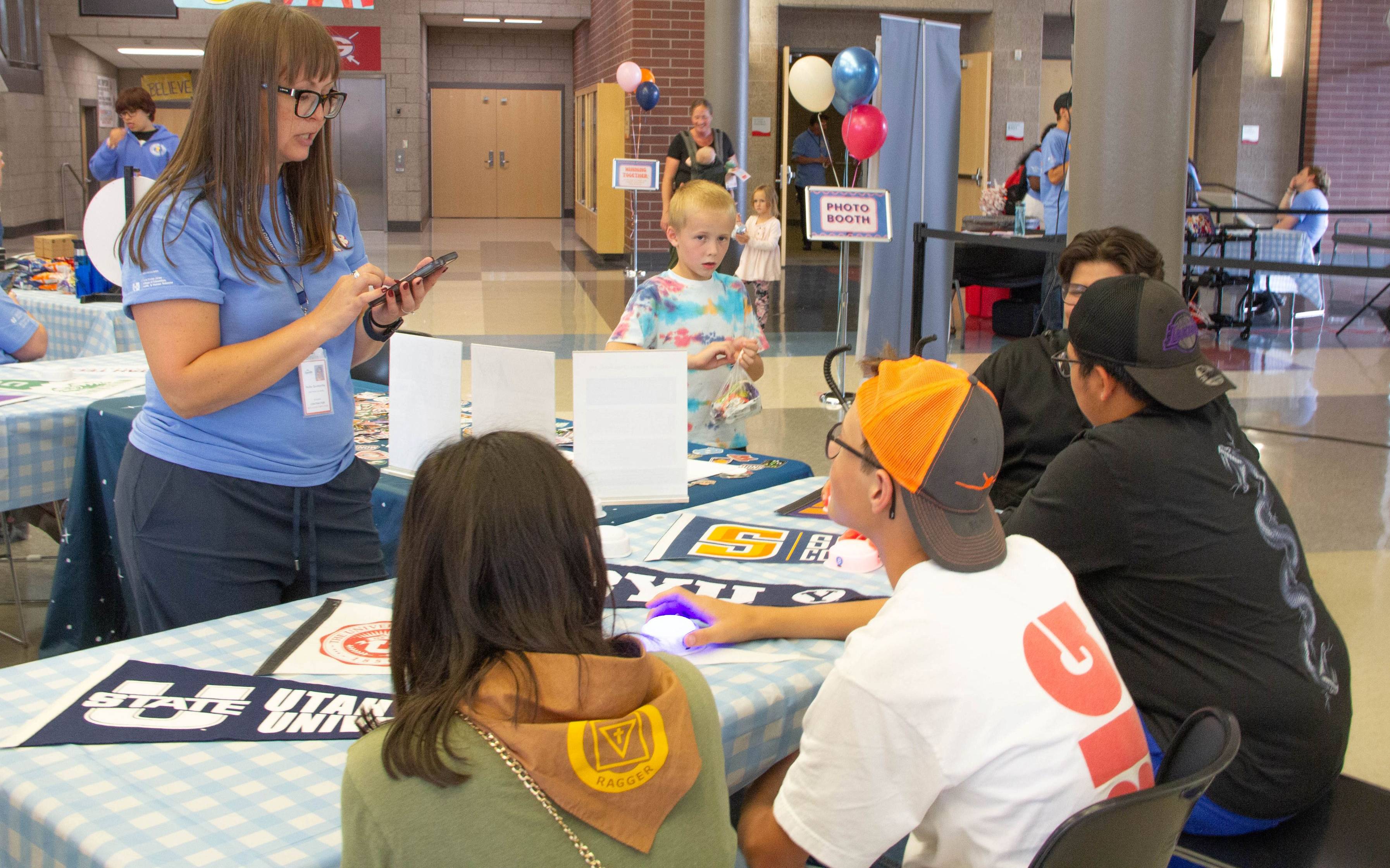 students and an advisor at a table, with the banners of various different colleges spread across the table