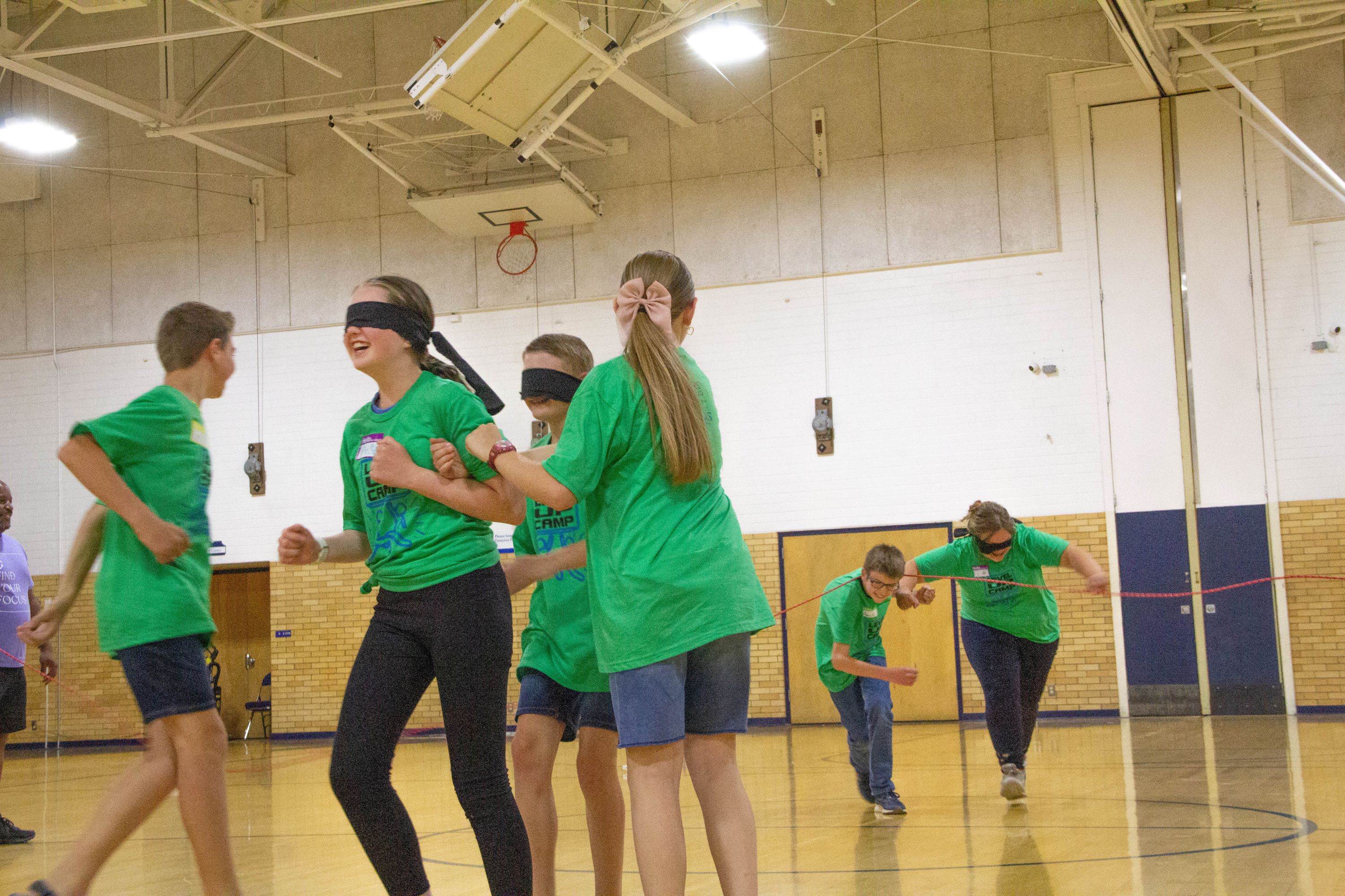 students wearing green shirts, laughing as they solve a blindfold challenge together